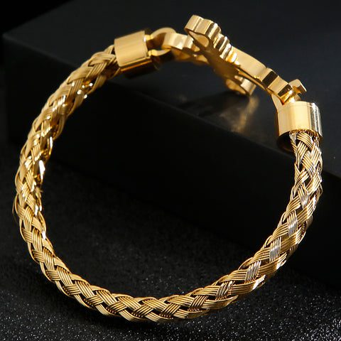 Bracelete dourado em fundo preto com detalhe da trama da pulseira.